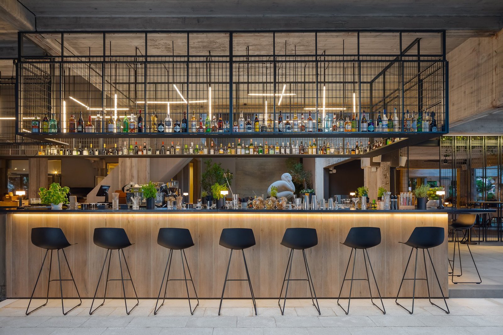 Sol Bar: lit timber bar with black stools under a steel bottle rack